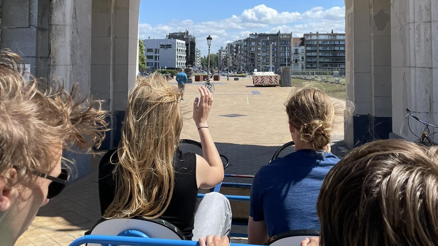 Deelnemers rijden met een meerpersoonsfietskar door een toegangspoort richting de zeedijk.