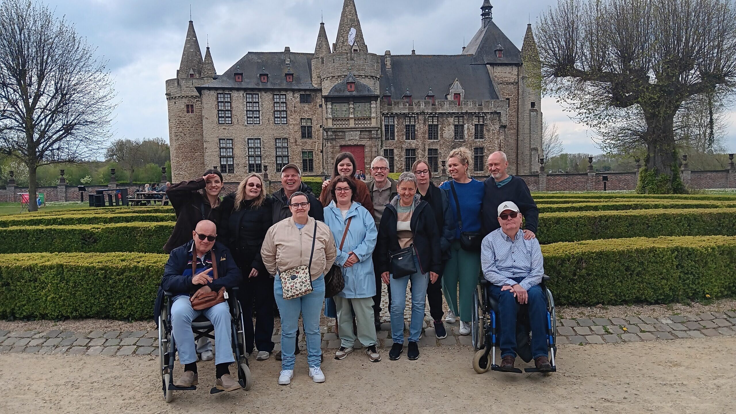 Groep bezoekers poseert voor een historisch kasteel met aangelegde tuinen tijdens een culturele uitstap.